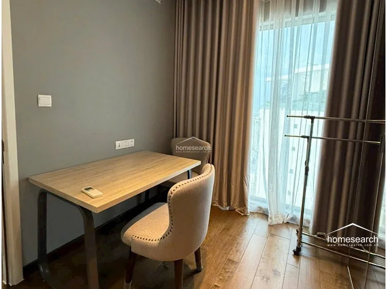 This functional workspace or secondary room is bathed in natural light filtered through soft, neutral-toned curtains. It is furnished with a minimalist desk, upholstered chairs, and wood flooring, maintaining the consistent, modern, and clean aesthetic found throughout the property.