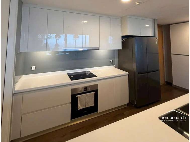 This view emphasizes the kitchen's streamlined layout, showcasing the seamless integration of the induction hob and stainless steel oven into the cabinetry. The grey glass backsplash provides a sophisticated touch, while the ample counter space and overhead storage cabinets offer high functionality for a modern home.
