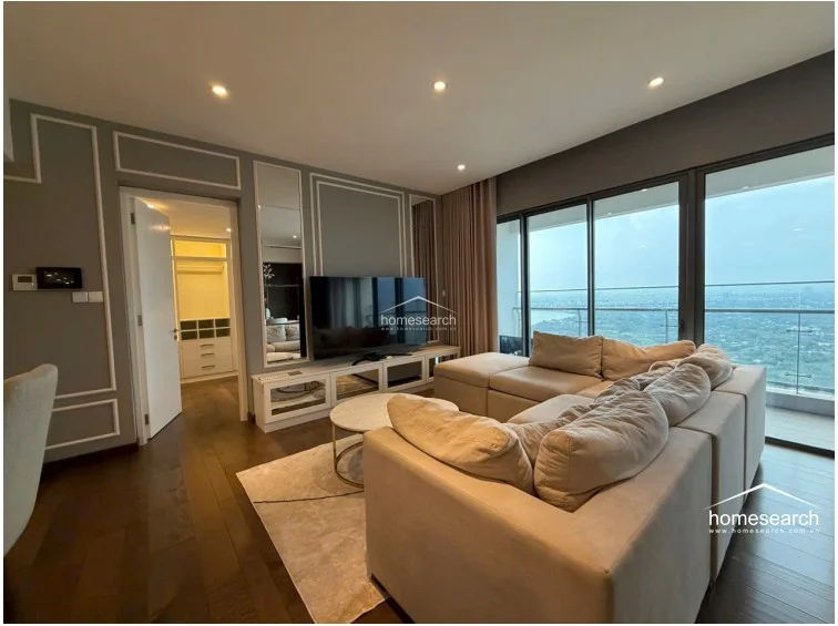The living room offers expansive floor-to-ceiling windows that provide a panoramic city view and flood the space with natural light. The room is finished with elegant crown molding, dark wood floors, and a neutral color palette, creating a cohesive and upscale atmosphere.