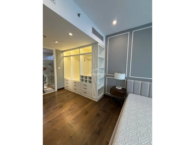 This bedroom features a custom, floor-to-ceiling white wardrobe with integrated open shelving and internal lighting for a luxurious, organized look. The room maintains a consistent design language with dark wood flooring, grey walls with white trim, and a high-end, modern aesthetic.