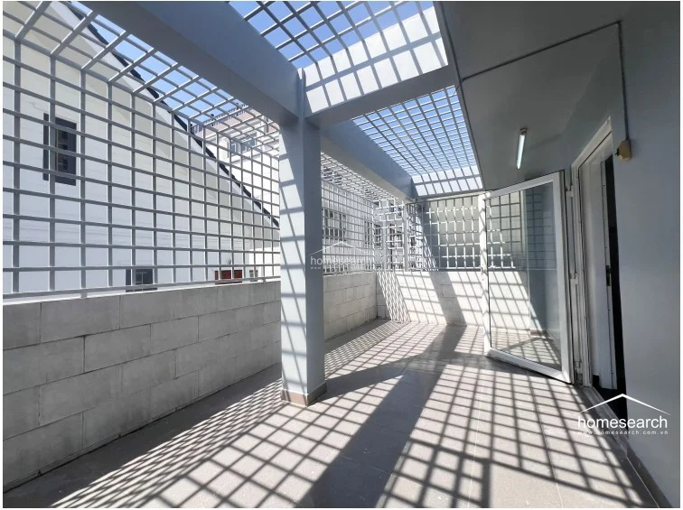 This covered outdoor terrace features a metal security cage enclosure and a concrete floor, offering a secure, semi-outdoor space. The area is accessed through a glass door and provides a functional, shaded environment for laundry or storage.
