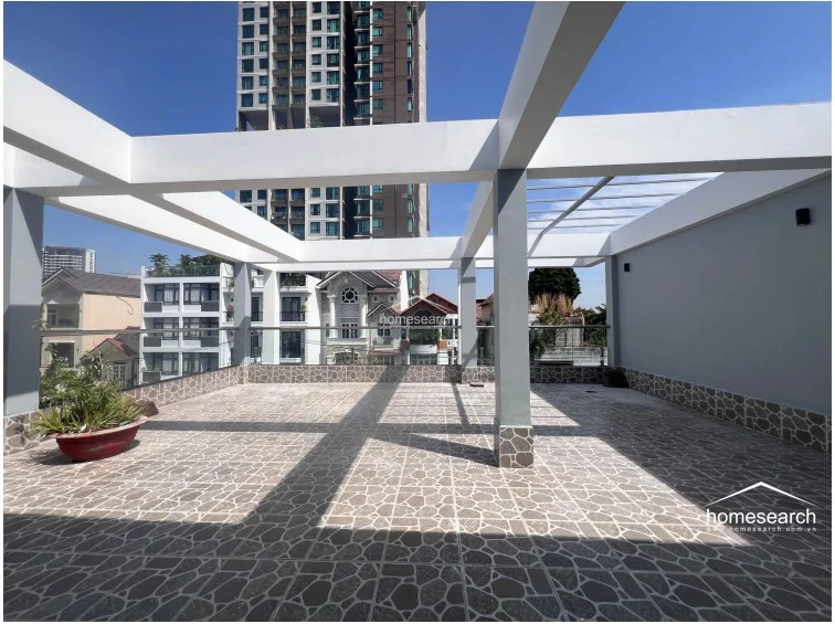 This expansive open-air rooftop terrace features decorative stone-patterned tile flooring and a sturdy concrete structural frame. It offers an unobstructed view of the surrounding urban landscape and provides a generous, versatile space for outdoor activities or gardening.