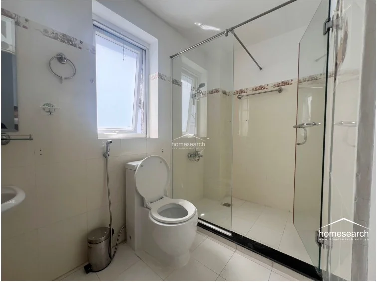 This bathroom is equipped with a glass-enclosed walk-in shower area and a modern white toilet. The space is brightened by a window and features neutral wall finishes, providing a well-maintained and practical layout.