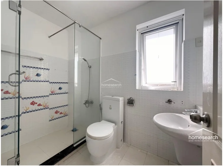 This bathroom features a glass shower partition accented with playful fish-themed decorative tiles on the interior wall. It includes a pedestal sink and a window, offering a bright, clean, and well-maintained environment.