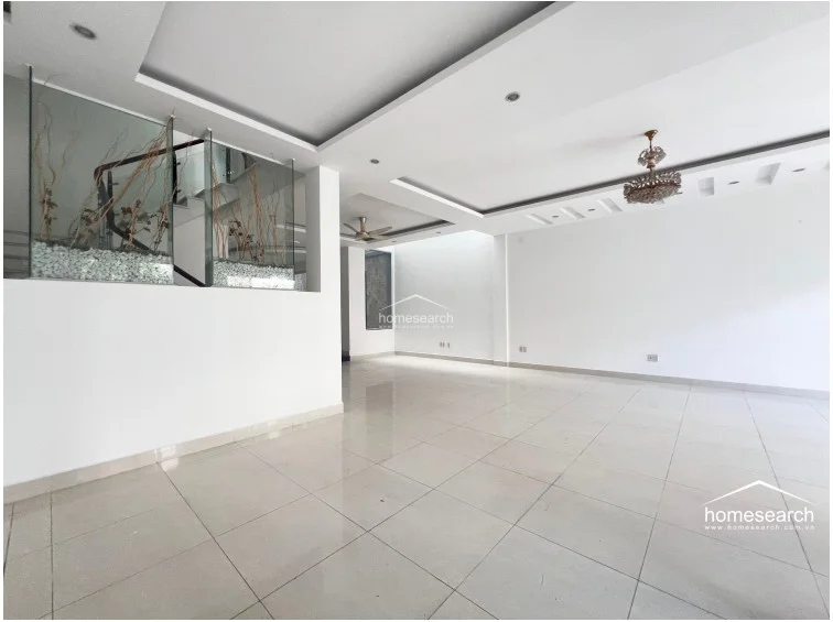 This view highlights the architectural layout of the living space, emphasizing the generous floor area and the decorative glass-enclosed planter feature near the staircase. The minimalist aesthetic and neutral color palette provide a versatile canvas, while the recessed lighting and clean lines reflect a modern, well-maintained interior.