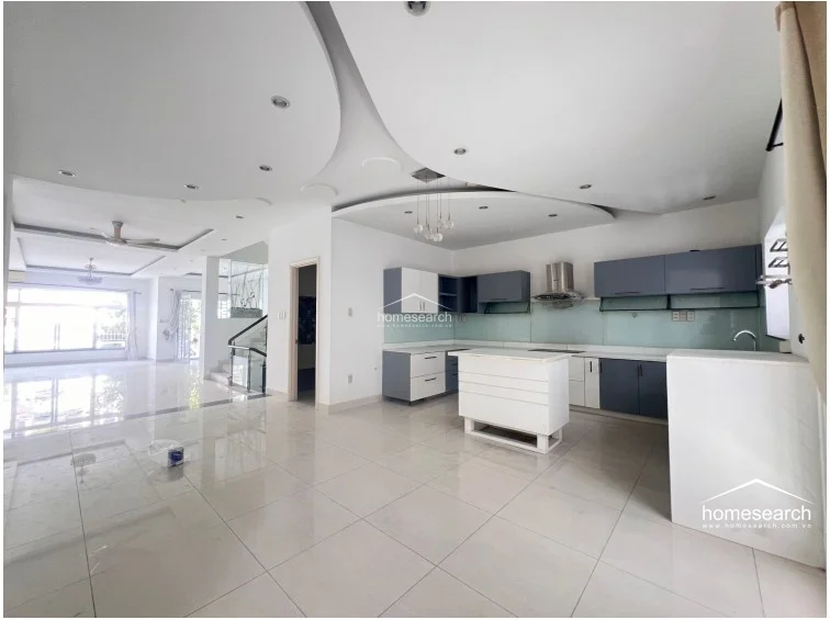 The kitchen is designed with a contemporary open-concept layout, featuring a central island and a sleek two-tone cabinetry scheme in white and slate blue. It is equipped with modern appliances, including a stainless steel range hood, and flows directly into the living area, making it ideal for entertaining.