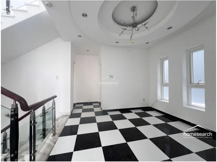 This view of the upper-level landing highlights the transition between the staircase and the interior rooms, emphasizing the cohesive design of the black-and-white flooring and recessed ceiling lighting. The open layout creates a sense of flow between the levels, with large windows providing ample natural light throughout the space.