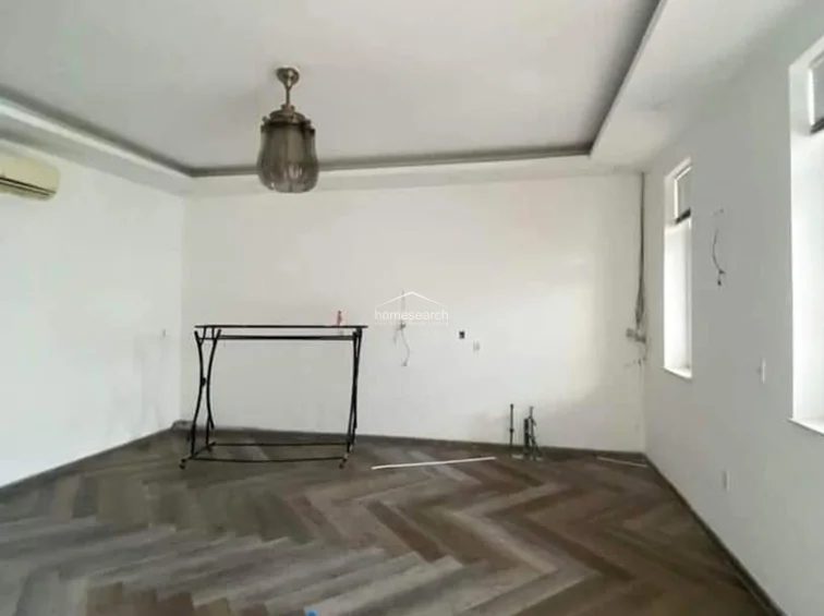 This living area features modern herringbone-patterned wood flooring and clean white walls, creating a bright and contemporary atmosphere. The space is equipped with a ceiling fan, an AC unit, and recessed lighting, though it currently remains unfurnished and awaiting final electrical finishes.