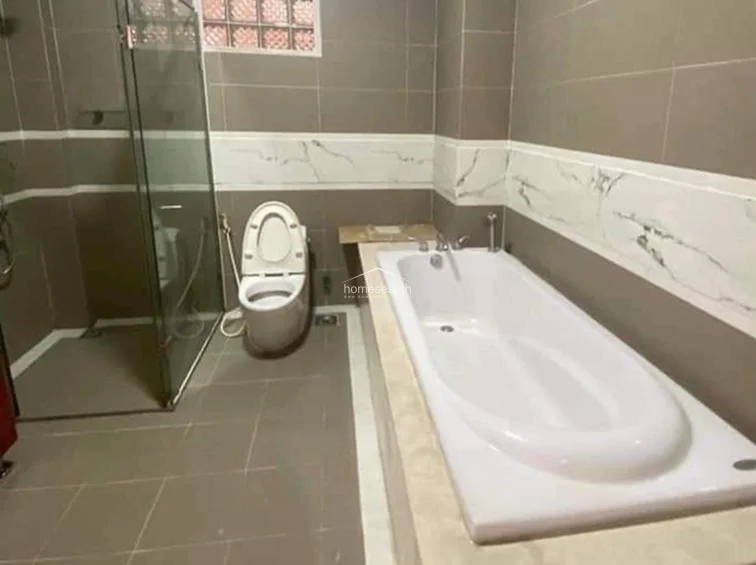 This spacious bathroom is designed with a separate glass-enclosed shower stall and a built-in soaking tub set into a marble-tiled deck. The room utilizes a sophisticated color palette of taupe and white marble accents, complemented by glass block windows that provide privacy while maintaining natural light.