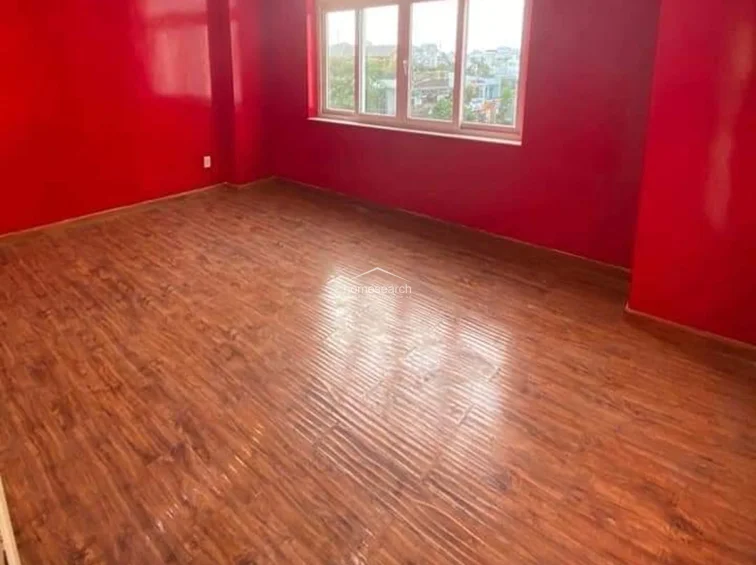 This bedroom is defined by its bold, vibrant red wall finish, which provides a striking contrast to the warm-toned wood-look flooring. Large windows allow for significant natural light and offer an elevated view of the surrounding neighborhood.