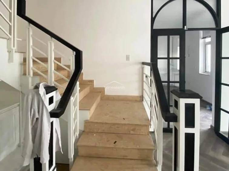 This interior staircase features a modern, high-contrast design with white walls, dark wood handrails, and black-framed glass doors. The landing area is finished with light-colored stone or tile steps, creating a sophisticated architectural transition between levels.