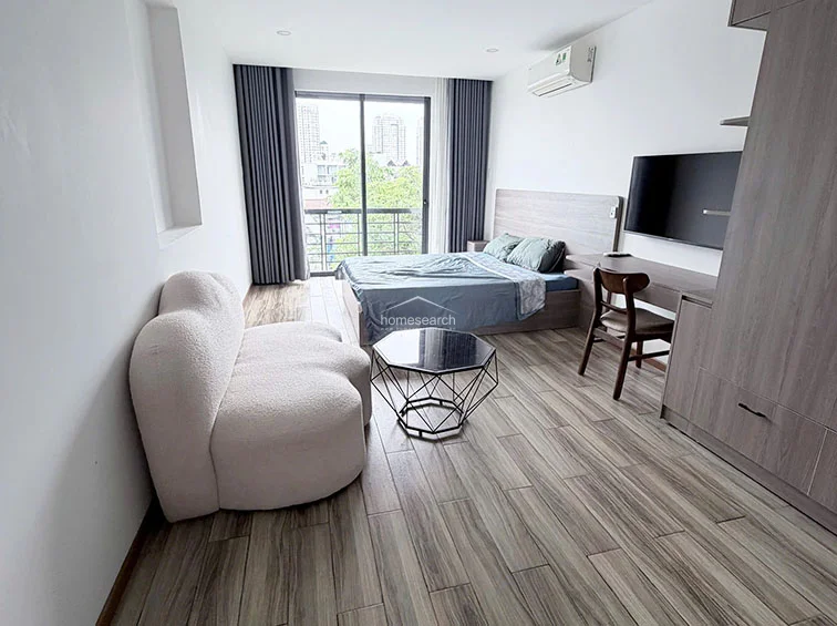 The perspective highlights the functional flow of the studio, showing the bedroom area transitioning toward the entryway and bathroom. The room is well-equipped with a split-system AC unit for climate control and a wall-mounted mirror that enhances the sense of space. The clean lines and minimalist built-in cabinetry provide efficient storage solutions while maintaining a contemporary aesthetic.