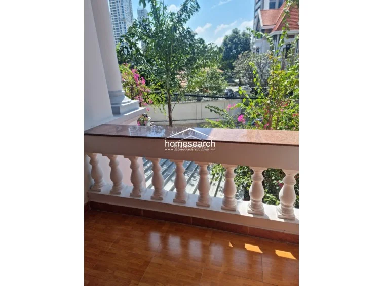 This outdoor balcony features a classic balustrade railing topped with a granite ledge, offering a pleasant view of the surrounding greenery and neighborhood. The floor is finished with warm-toned wood-look tiles, creating a comfortable and inviting space for outdoor relaxation.