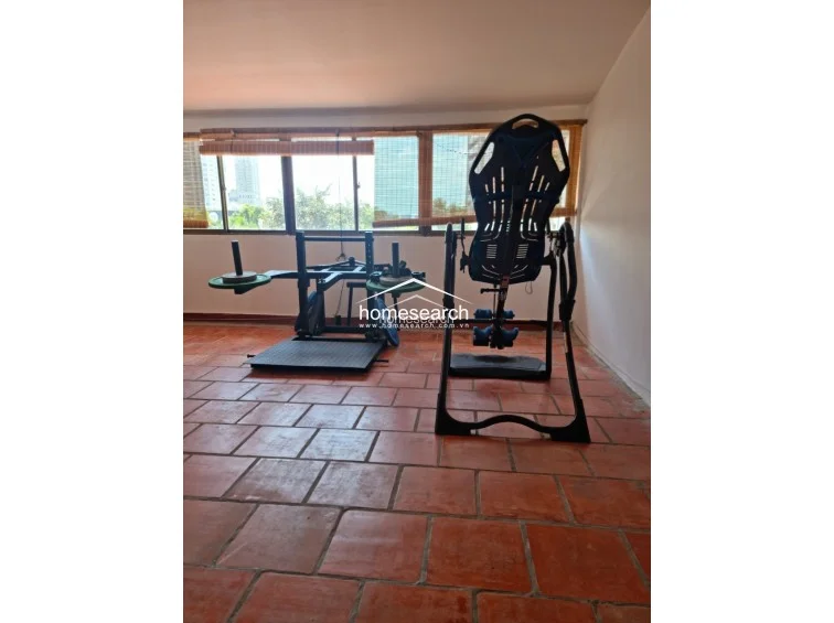 This area serves as a dedicated fitness zone, showcasing a spacious layout that accommodates multiple exercise machines, including an inversion table. The room maintains a consistent design with the rest of the property, utilizing terracotta tile flooring and natural light filtered through window blinds.
