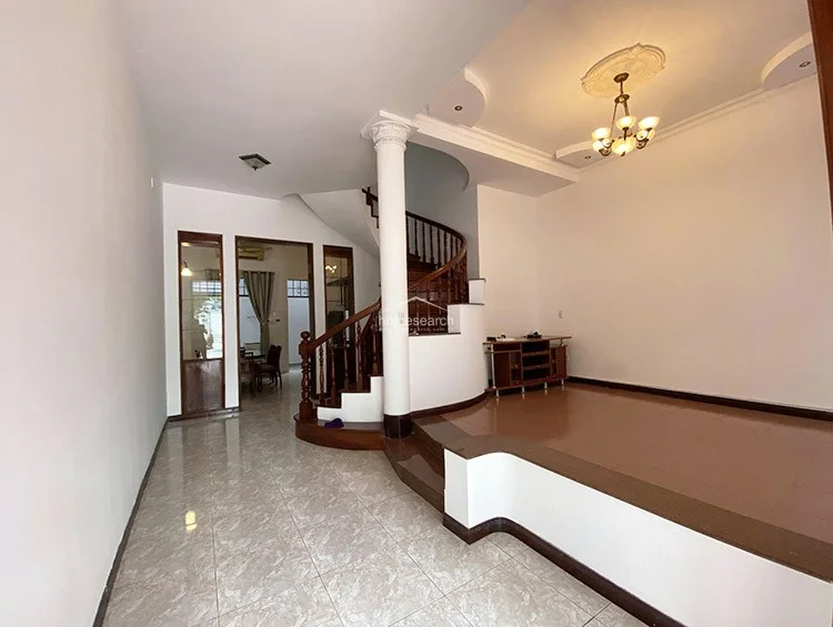 This transition space features light-colored floor tiles and leads directly to an outdoor balcony through a wooden-framed glass door. The area is brightened by natural light from the balcony and a high transom window, maintaining a clean, minimalist aesthetic with white walls.