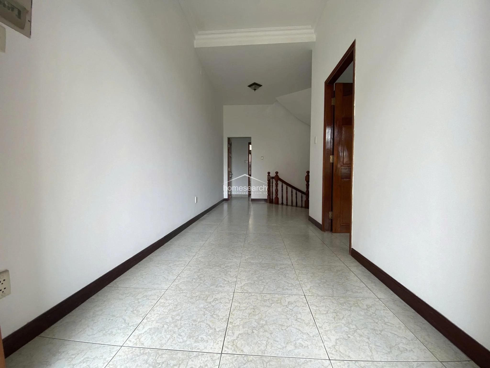 This image shows a spacious, neutral-toned hallway with light-colored marble-effect floor tiles and white walls. It features a traditional wooden door frame and connects to other rooms, maintaining a clean and well-maintained appearance.