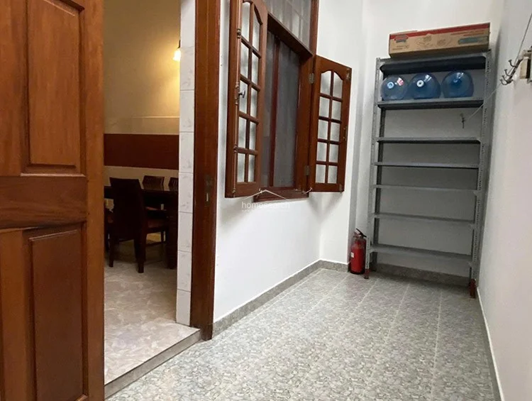 This utility or transitional space features durable speckled tile flooring and white walls, providing a clean, functional area. It includes a metal shelving unit for storage and a wooden window that opens into the adjacent dining room, allowing for natural light and airflow.