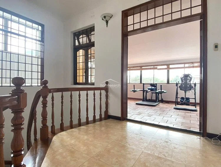 This transition space leads directly into a dedicated fitness area through a wide, open doorway framed in dark wood. The landing features light-toned floor tiles and a wall-mounted light fixture, providing a clear visual flow between the interior circulation and the specialized gym room.