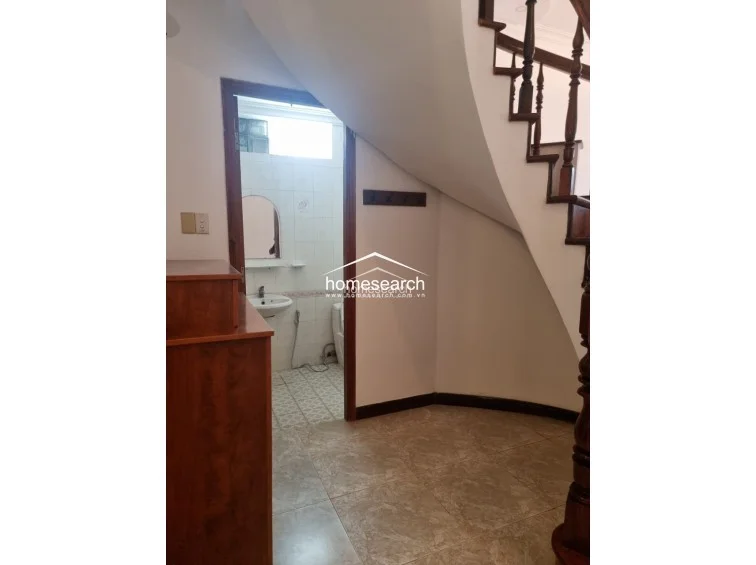 This area is located beneath the staircase, utilizing the architectural void to house a compact, functional guest bathroom. The space features simple tiling and basic fixtures, connecting directly to the main living area through an open doorway.