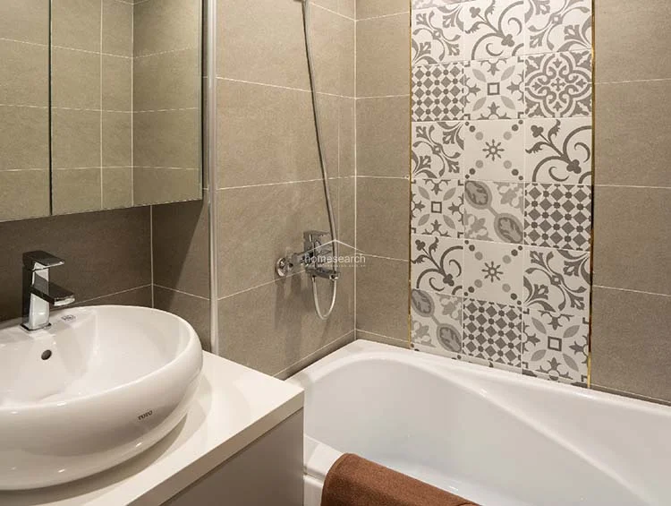 This bathroom highlights a contemporary design with a combination of solid grey wall tiles and a decorative, patterned accent strip above the bathtub. It is equipped with a modern white vessel sink, a mirrored medicine cabinet, and high-quality fixtures, maintaining a polished and well-maintained appearance.