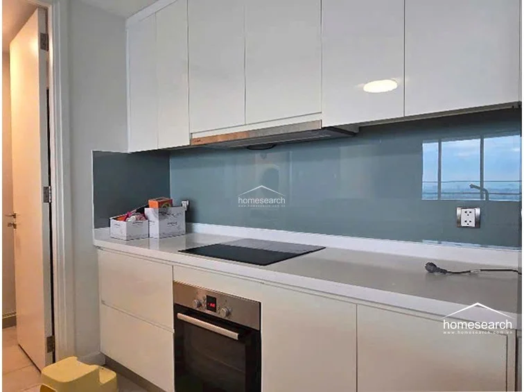 This modern kitchen features high-gloss white cabinetry, a clean white countertop, and a sleek grey glass backsplash that reflects the natural light. It is equipped with integrated appliances, including a built-in oven and induction cooktop, maintaining a clutter-free and highly functional workspace.