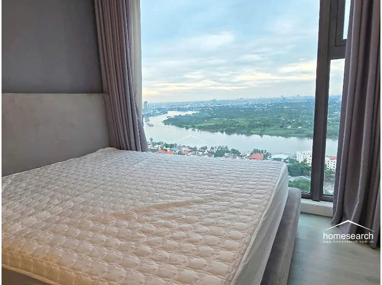 This angle emphasizes the bedroom's connection to the scenic outdoor environment, with the bed positioned to take full advantage of the river views. The room is well-maintained, featuring quality window treatments and a clean, modern design that emphasizes the height of the windows.