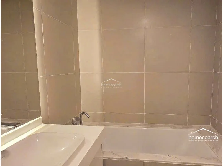 This bathroom features a clean, minimalist design with large-format beige wall tiles and a white vanity countertop. It includes a built-in bathtub with a modern chrome faucet, reflecting a well-maintained and contemporary aesthetic.