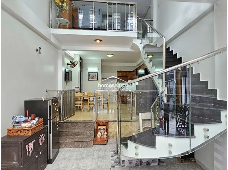 This view captures the open-plan ground floor, which transitions from a front entrance area to a raised dining and kitchen space. The interior features a striking curved staircase with glass railings and dark stone treads, creating a contemporary flow between levels.