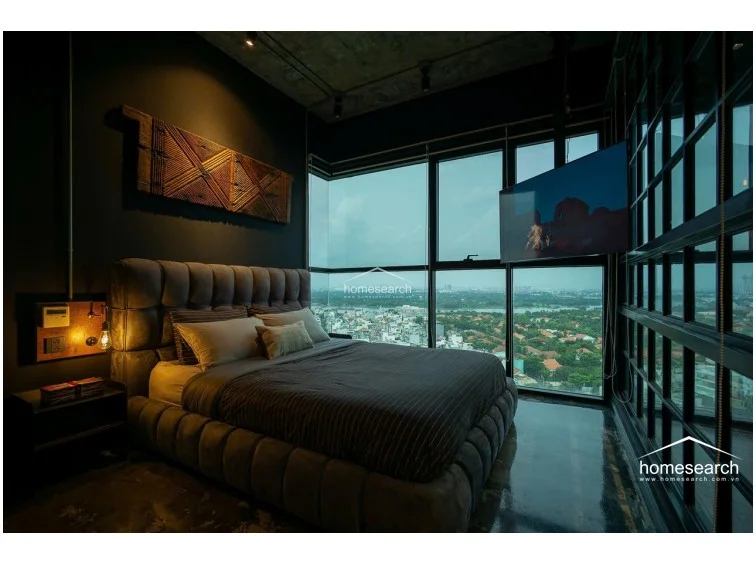 This bathroom is defined by its dramatic all-black tile finish and industrial fixtures, including a rustic wooden vanity top and a copper-toned basin. The space is cleverly designed with an open-concept feel, utilizing a glass partition to maintain a connection with the bedroom while offering a unique, elevated shower experience.