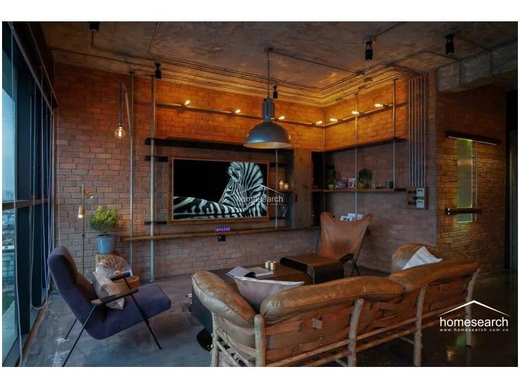 The open-concept kitchen and living area maintains a cohesive industrial aesthetic with exposed ceiling ductwork and metal conduit lighting. The kitchen is equipped with a substantial wooden-topped breakfast bar and high-end built-in appliances, seamlessly flowing into the lounge area.