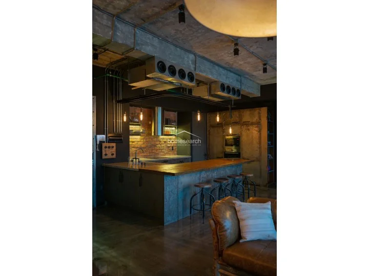 This cozy bedroom continues the industrial theme with a feature wall of exposed brick and a striking matte black accent wall. It includes a custom floor-to-ceiling wooden wardrobe and a built-in desk area, maximizing storage and functionality within the compact footprint.