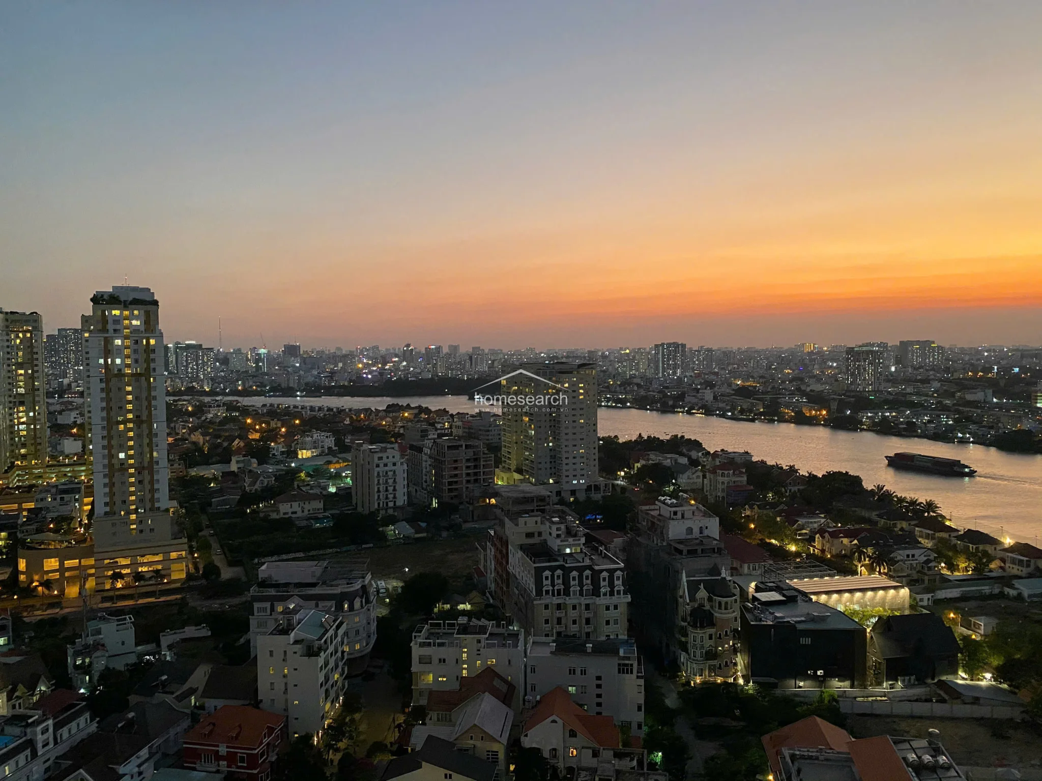 This high-rise apartment offers a stunning, unobstructed panoramic view of the city skyline and river, captured during a vibrant sunset. The perspective highlights the density of the surrounding urban landscape and the tranquil water feature, suggesting a prime, elevated location.