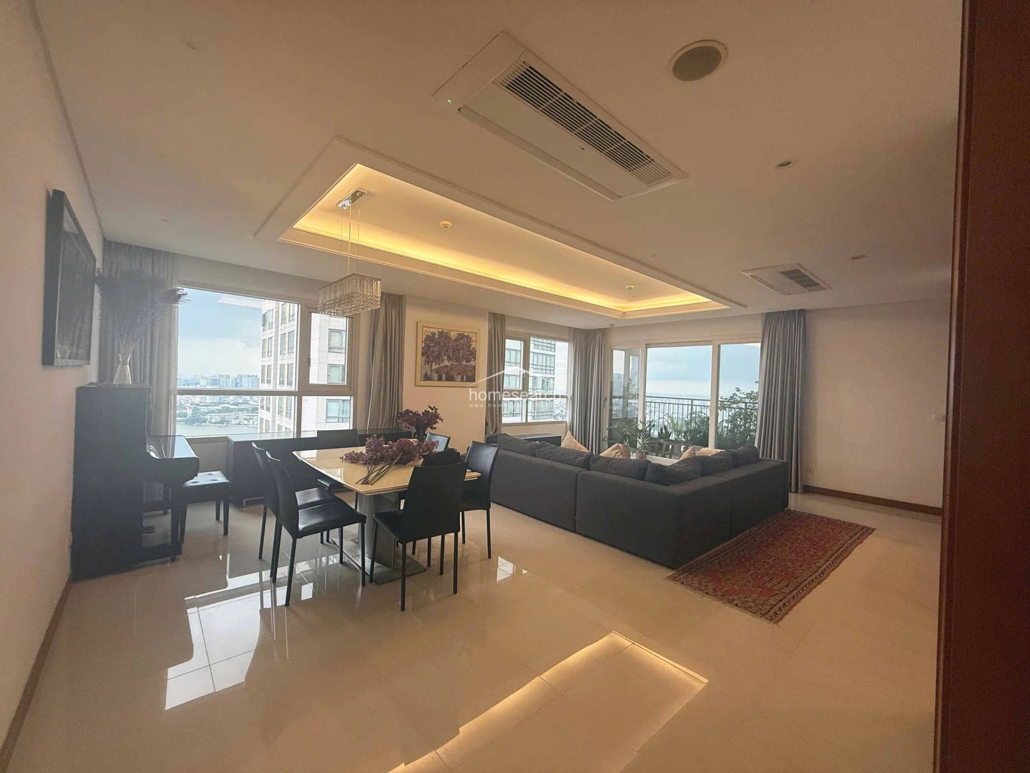 This view highlights the spacious layout, showcasing a dining set positioned near a black piano and a large window that frames the urban landscape. The high-end finishes, including the crystal chandelier and recessed lighting, emphasize the well-maintained, contemporary condition of the property.
