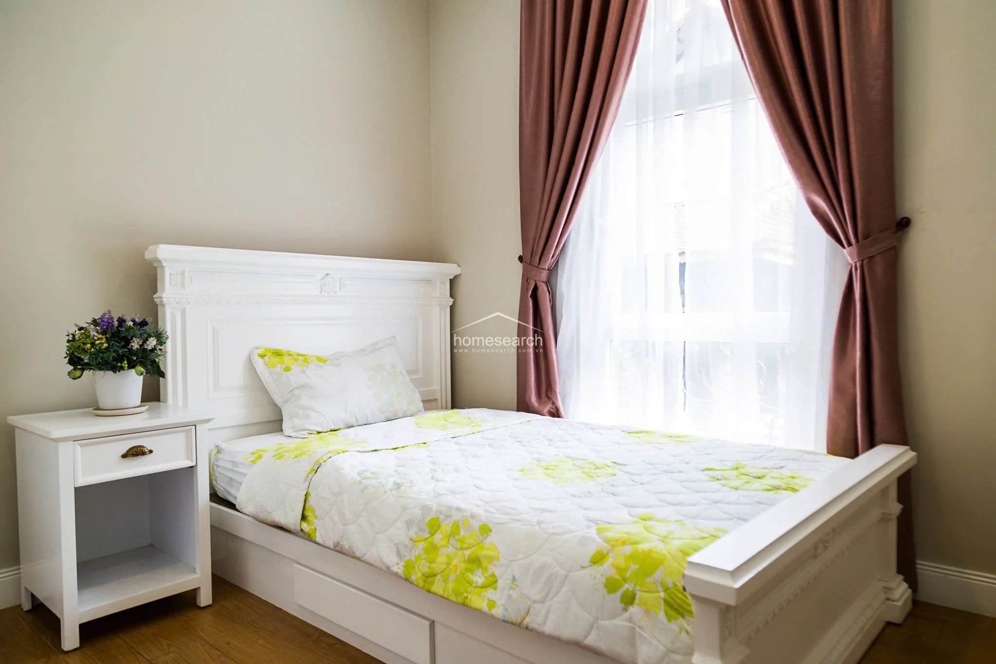 This bedroom is identical to the previous one, maintaining a consistent design theme with its white furniture and soft, inviting color palette. The room is well-lit by natural light filtering through the sheer and heavy curtains, highlighting the clean, neutral wall finish.
