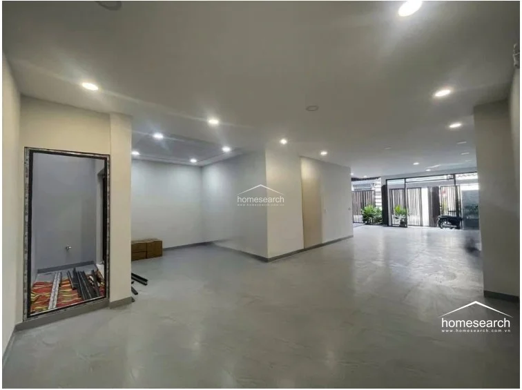 The interior is an expansive, open-plan ground floor space characterized by polished concrete-style flooring and a neutral white color palette. Recessed ceiling lights provide ample illumination, while the layout flows directly toward the front entrance, suggesting a versatile area suitable for a living room, showroom, or garage space.
