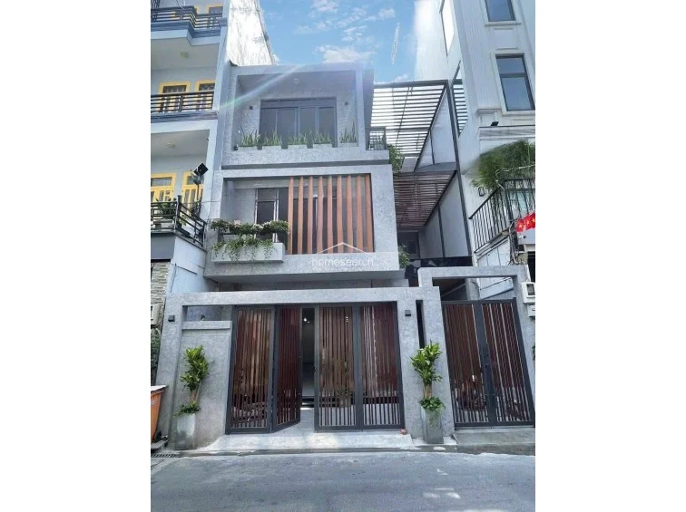 This modern multi-story townhouse features a contemporary facade with textured grey concrete finishes and vertical wooden slat accents. The design incorporates integrated planter boxes on the balconies and a sleek metal gate, showcasing a high level of maintenance and a sophisticated, minimalist aesthetic.