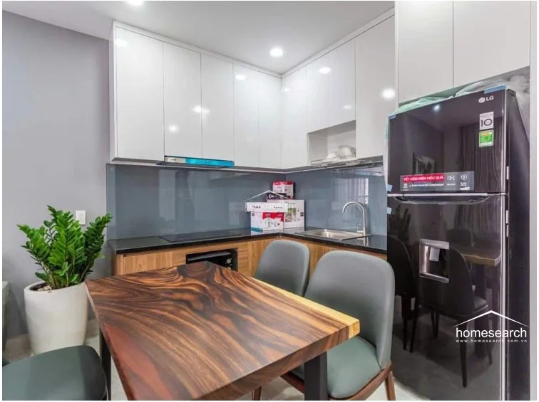 The dining area serves as a transition point between the living room and the kitchen, anchored by a unique live-edge wood table and four grey upholstered chairs. The space feels cohesive and functional, with the kitchen's compact design maximizing the utility of the open floor plan.