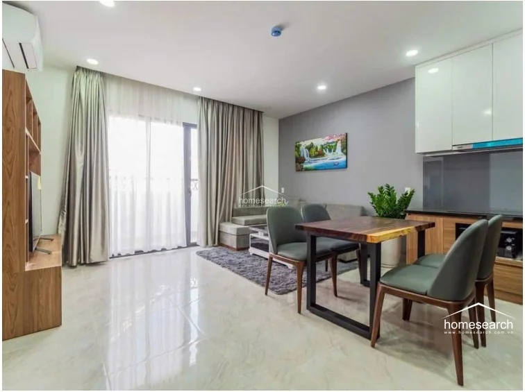 This open-concept living and dining area features polished light-toned tile flooring and a modern, neutral color palette with a grey accent wall. The space is well-lit by recessed ceiling lights and large floor-to-ceiling glass doors that lead to a balcony, providing ample natural light.