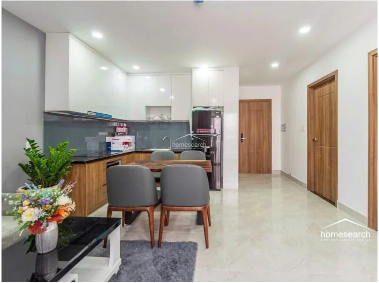 The kitchen area is efficiently designed with an L-shaped layout, featuring high-gloss white upper cabinetry and wood-tone lower cabinets. It is equipped with a dark countertop, a grey glass backsplash, and a full-sized black LG refrigerator, all appearing modern and well-maintained.