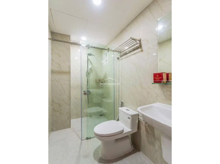 This bathroom is finished with elegant, light-veined marble-style wall tiles and features a modern glass-enclosed walk-in shower. The space is efficiently laid out with a wall-mounted sink, a sleek toilet, and a stainless steel towel rack, all appearing to be in well-maintained condition.