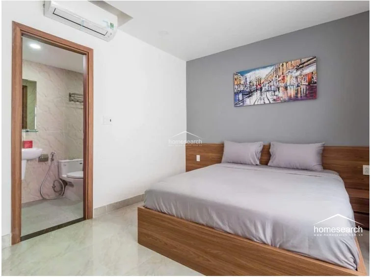 This bedroom connects directly to an en-suite bathroom, which features marble-patterned wall tiles and standard sanitary fixtures. The room is equipped with a wall-mounted AC unit, recessed ceiling lighting, and a modern, minimalist aesthetic with a grey accent wall.