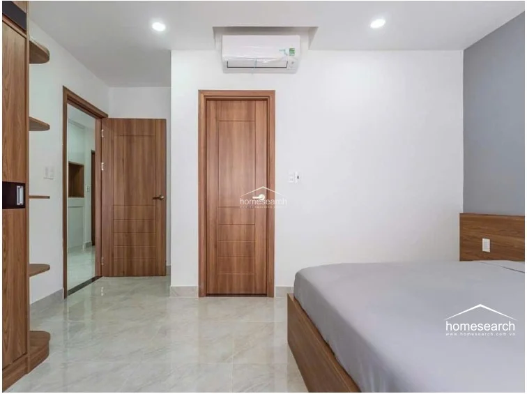 This bedroom provides a clear view of the interior flow, showing access to both a hallway and an attached bathroom through matching wooden doors. The room is well-appointed with a wall-mounted AC unit, recessed lighting, and a large wooden wardrobe, reflecting a high level of maintenance and modern design.