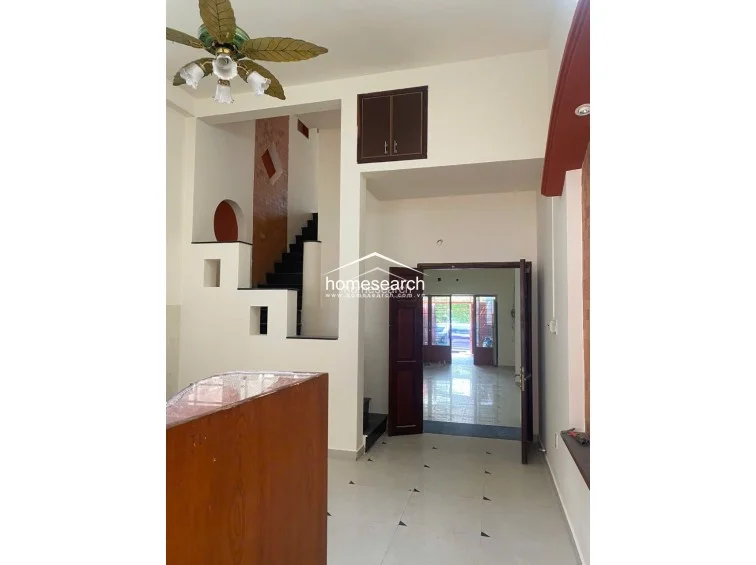 This interior view highlights the staircase area, which features a unique decorative brick accent wall and a ceiling fan with leaf-shaped blades. The layout includes a built-in overhead storage cabinet and an open flow that connects the front entrance area to the rear of the house.