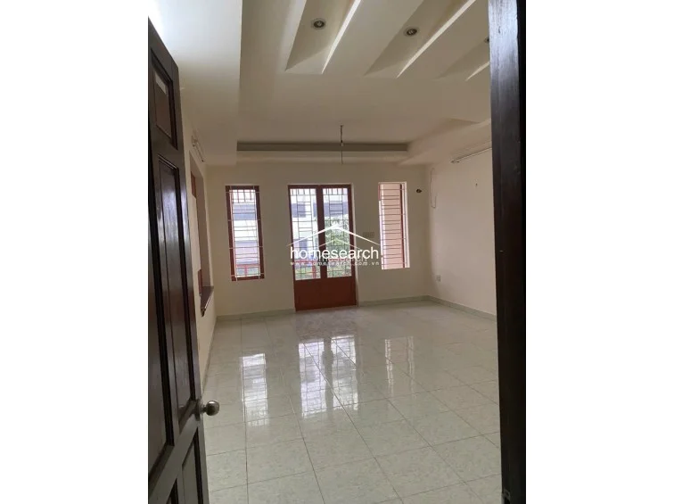 This room features a sophisticated tray ceiling with recessed lighting and large windows that provide ample natural light and ventilation. The space is finished with light-colored tile flooring and neutral walls, offering a versatile layout suitable for a bedroom or living area.