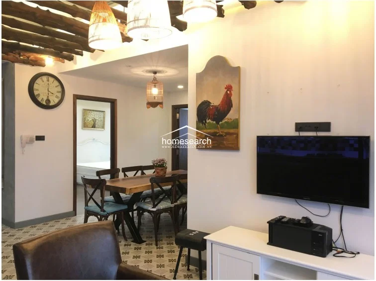 The living room layout centers around a wall-mounted television and a white media console, flanked by two charming rooster-themed wall plaques. The area maintains a cohesive design language with the rest of the home, utilizing the same patterned tile flooring and warm, inviting lighting fixtures.