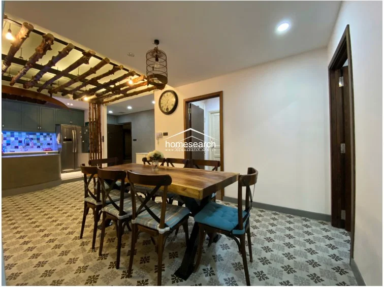 This view highlights the kitchen's functional layout, featuring muted green cabinetry and a striking multi-colored mosaic tile backsplash. A curved, concrete-topped breakfast bar separates the kitchen from the living area, and a decorative wooden boat fixture hangs above, emphasizing the home's distinct, curated aesthetic.