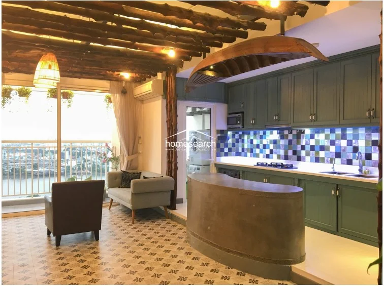This wide-angle shot showcases the seamless integration of the kitchen and lounge, highlighting the high-contrast design elements like the dark wood ceiling and the sleek, modern concrete bar. The space feels well-maintained and thoughtfully designed, maximizing the flow between the indoor living area and the adjacent balcony.