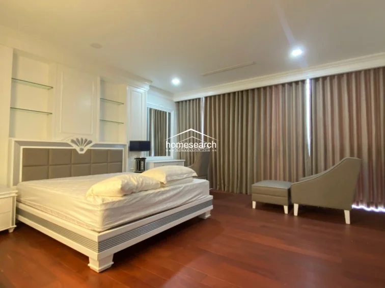 This bedroom is finished with warm-toned hardwood flooring and features a large, modern bed frame with integrated bedside shelving. A wall of floor-to-ceiling curtains provides privacy and soft natural light, while a neutral color scheme and minimalist furniture create a calm, well-maintained atmosphere.