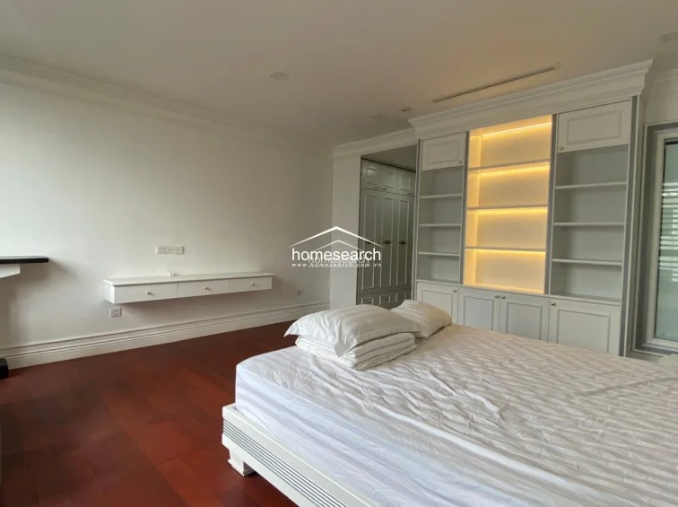 This bedroom area highlights a minimalist design with rich dark wood flooring and a wall-mounted floating console for storage. The space features extensive built-in white cabinetry and open shelving with integrated warm lighting, providing both functionality and a cozy atmosphere. The room is clean and well-maintained, emphasizing a modern and clutter-free environment.
