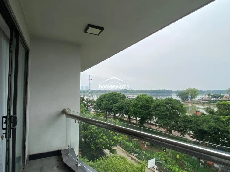 This private balcony offers a serene, elevated view of a lush green landscape and a nearby river. It is finished with neutral-toned floor tiles and a minimalist glass railing, providing a clean, unobstructed connection to the outdoors.